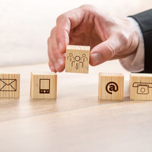 Close up Businessman Arranging Wooden Cubes with Contact and Customer Care Symbols on Top of a Table.